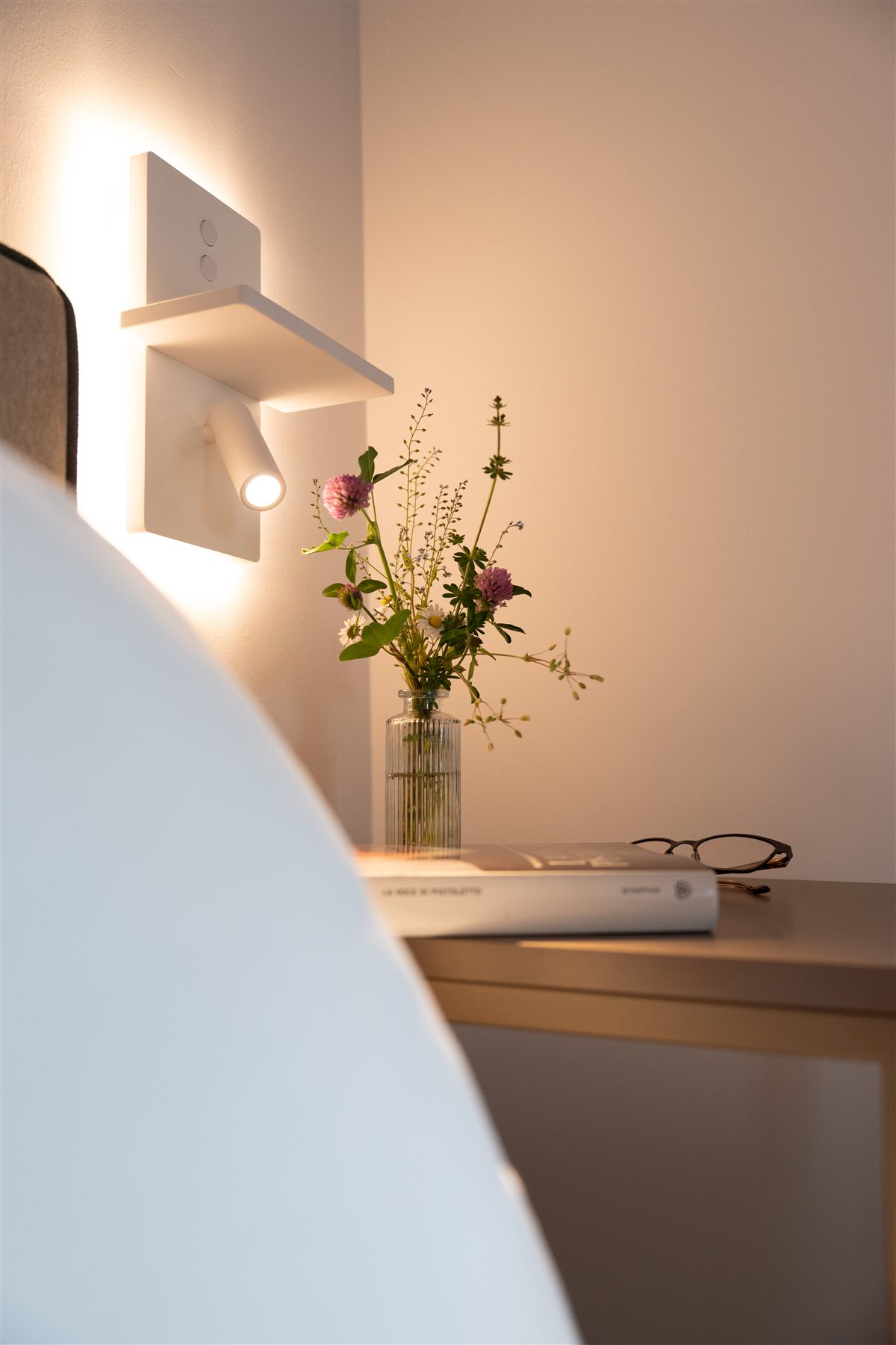 Dettaglio bedside con libro, occhiali e vaso.